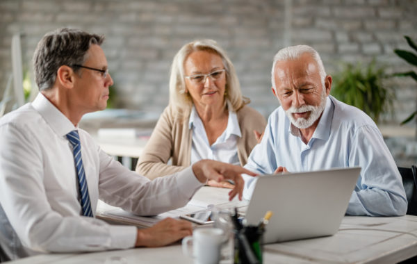 Mature couple and insurance agent using computer during consultations in the office.